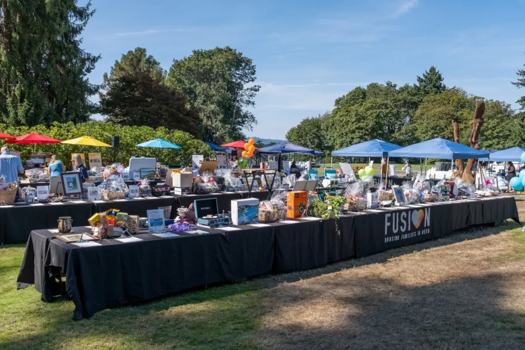 FUSION outdoor fundraiser: long tables with auction items under colorful umbrellas and blue tents.