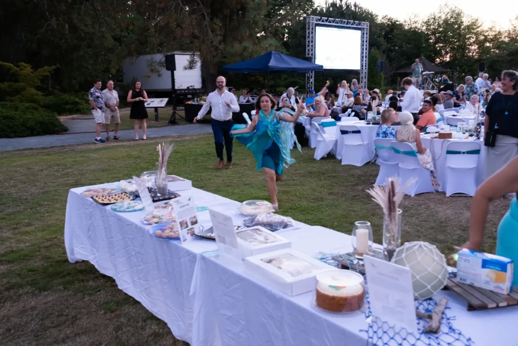 Woman in a flowing blue dress dances at a festive outdoor evening event with dessert tables.