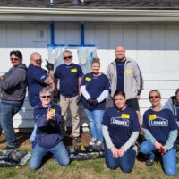 Smiling, diverse Lowe's volunteers pose outdoors with tools and mulch bags for a project.