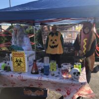 Outdoor Halloween event featuring costumed scientist, pumpkin, hot dog at a spooky science table.